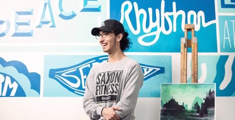 Art student stood in front of art display of their work.