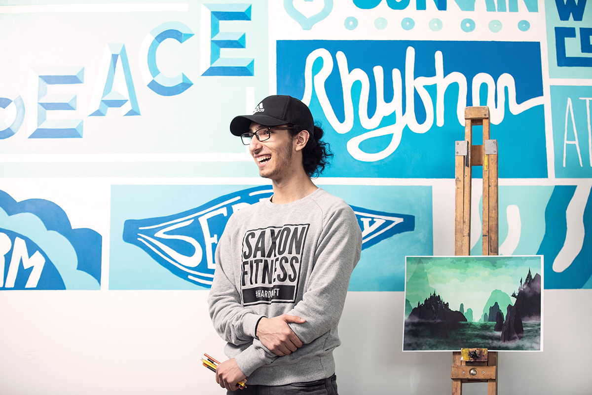 Art student stood in front of art display of their work.