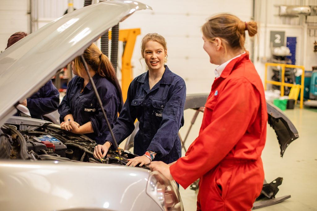 Female automotive students around a car engine