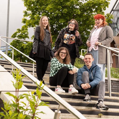Group of students stood outside on stairs laughing with each other