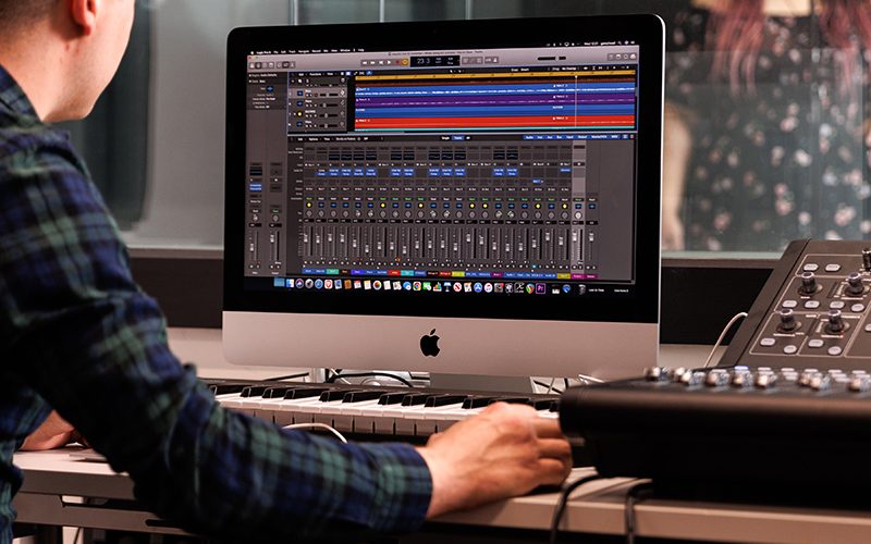 Music production studio desk with a singer in the soundbooth