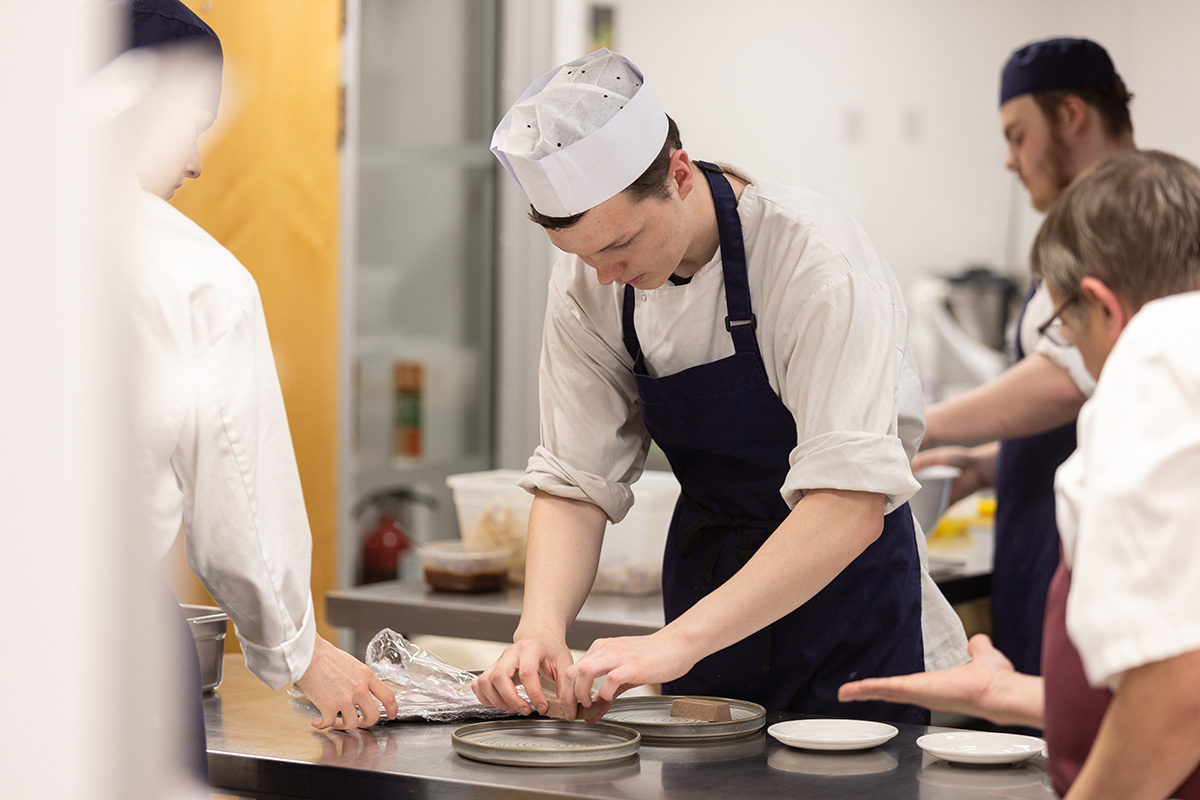 Student plating dish in kitchen