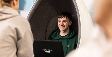Student sat in a pod chair working on a laptop