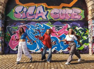 Three dancers dancing in front of a grafitti covered wall