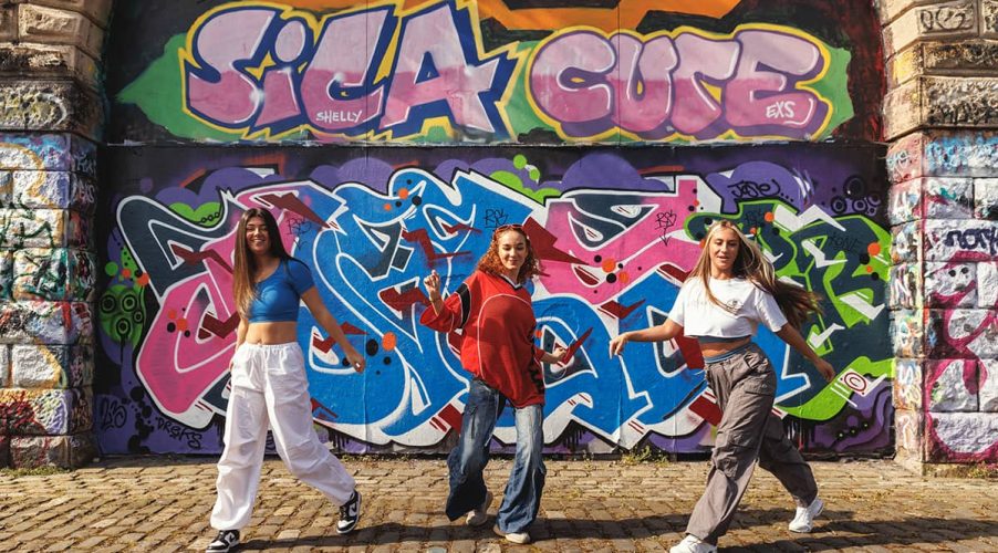 Three dancers dancing in front of a grafitti covered wall