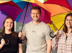 Gateshead Colleges School Liason Team smiling to camera, holding rainbow coloured umberellas