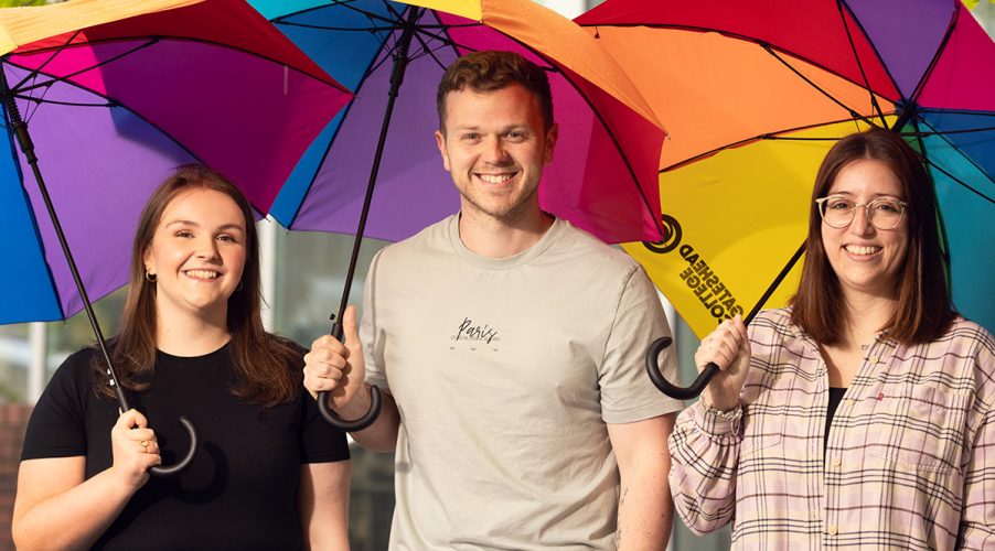 Gateshead Colleges School Liason Team smiling to camera, holding rainbow coloured umberellas