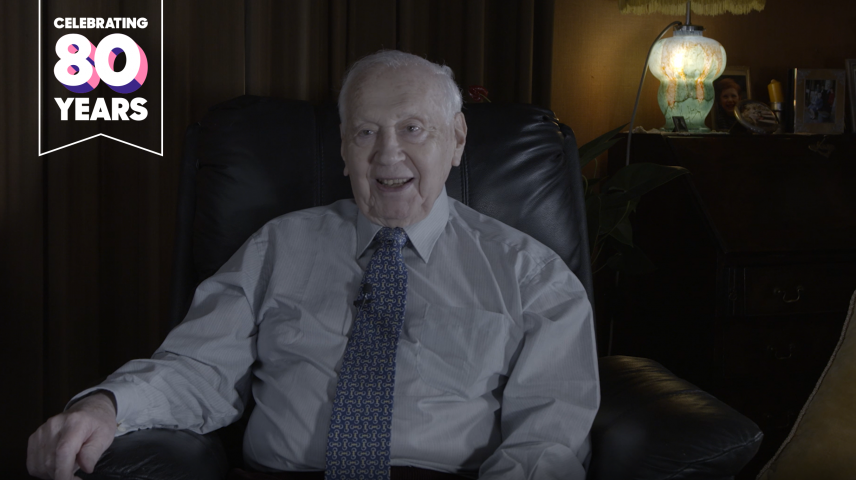 An elderly man sitting smiling on a sofa