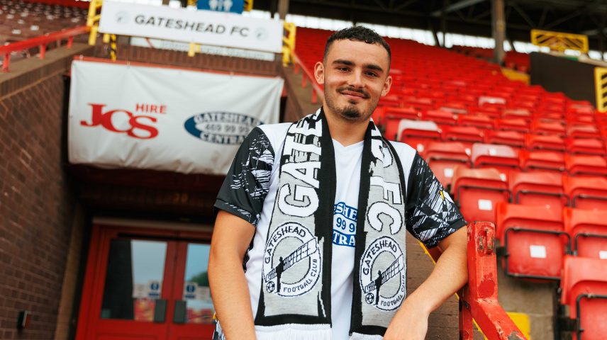A young man stands in the stands of a football ground.