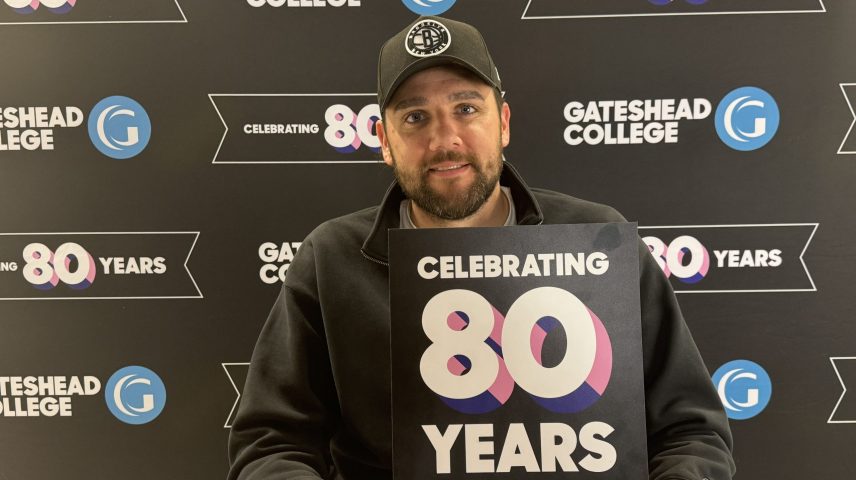 A man wearing a cap holding a sign saying Celebrating 80 Years
