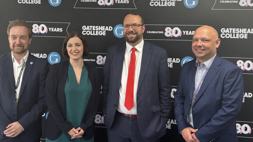 Four people standing smiling infront of a banner that says 'Gateshead College 80 years'