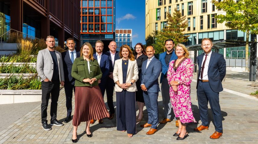 A group of men and women standing outside on a sunny day.