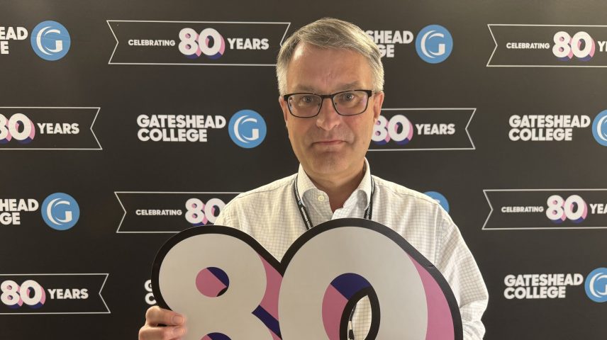 A man with glasses standing holding a large number eighty