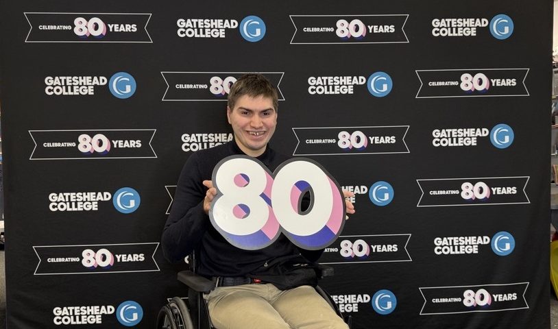 A man sitting in a wheelchair holding a large 8 and 0 in his hands.