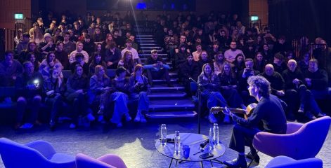 A group of people watching someone sing and play guitar in a theatre