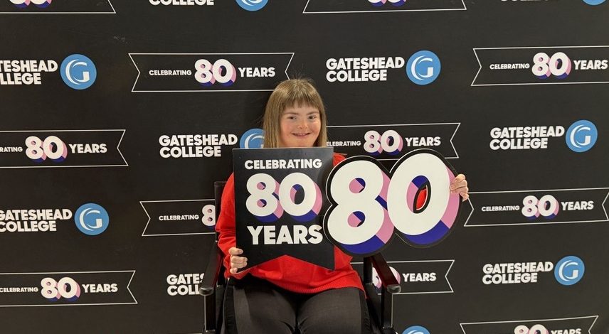 A lady sitting holding a giant 80 and a sign saying celebrating 80 years