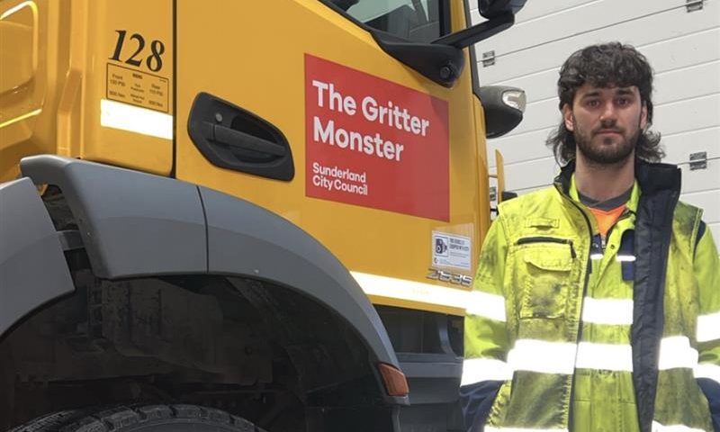 A man in high vis workwear standing infront of a gritter.