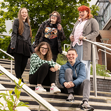 Group of students stood outside on stairs laughing with each other.
