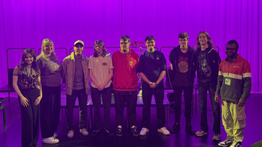 A group of people standing on a stage under a pink light.