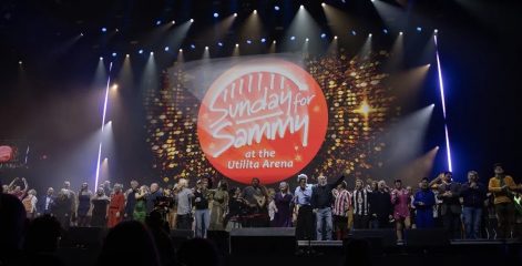 A group of performers standing on a stage that says 'Sunday for Sammy 26'