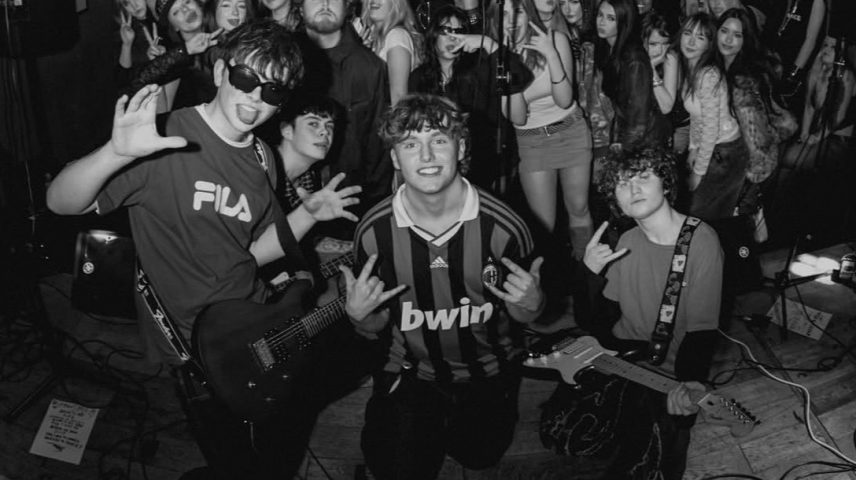 A band on stage with fans behind them.