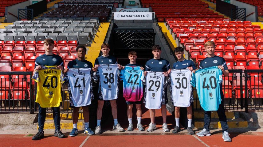 A group of footballers standing holding football shirts up.